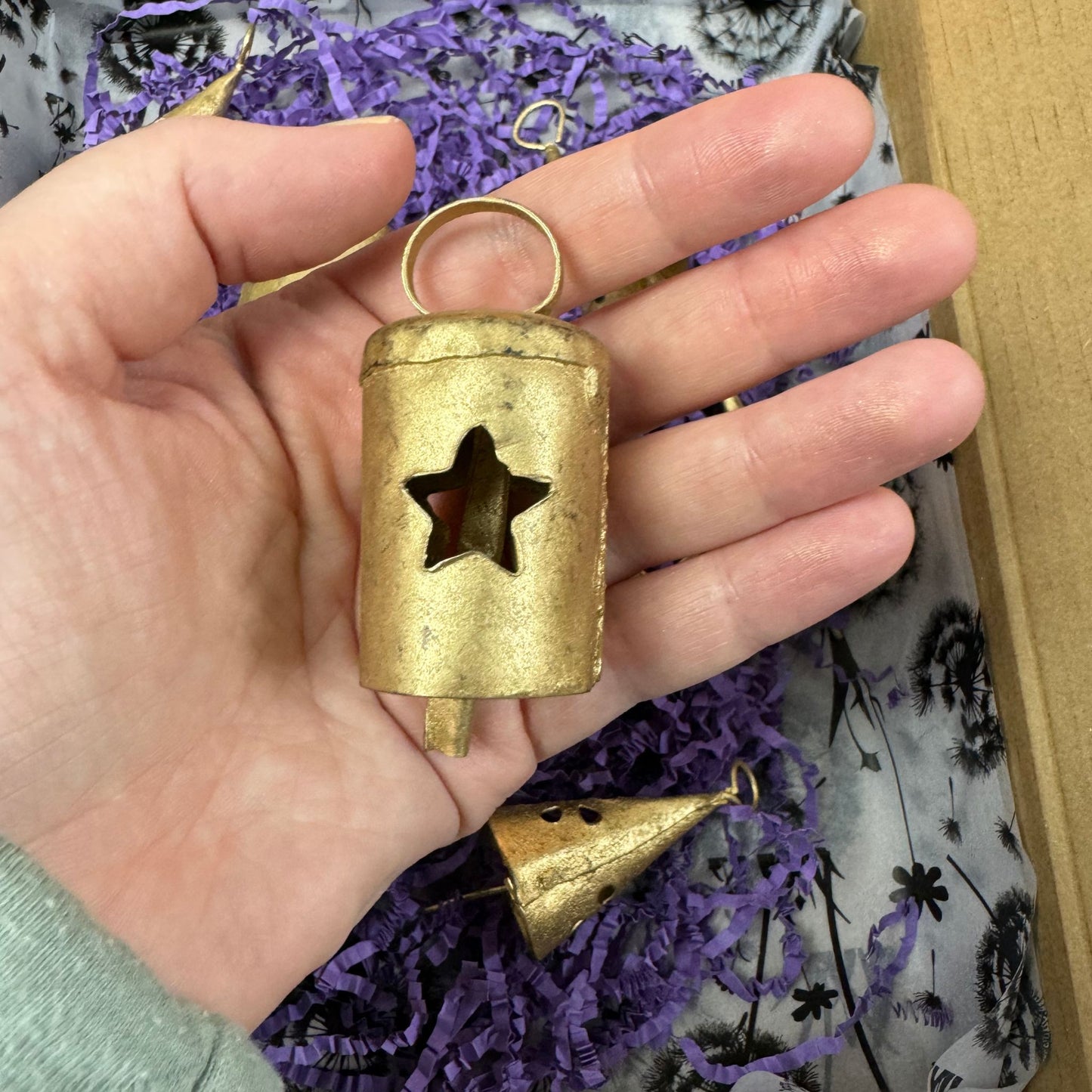 Hand holding a small gold bell with a star cutout against a textured purple and gray background.