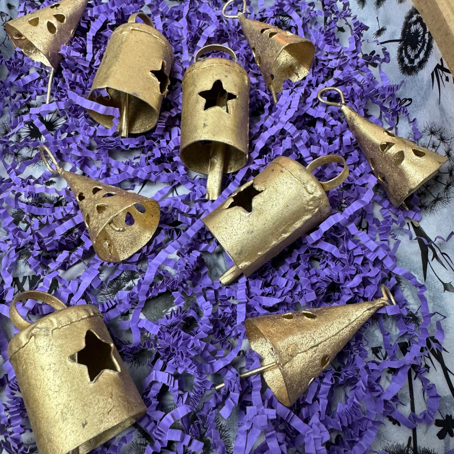 Gold tin bells with star cutouts on purple shredded paper