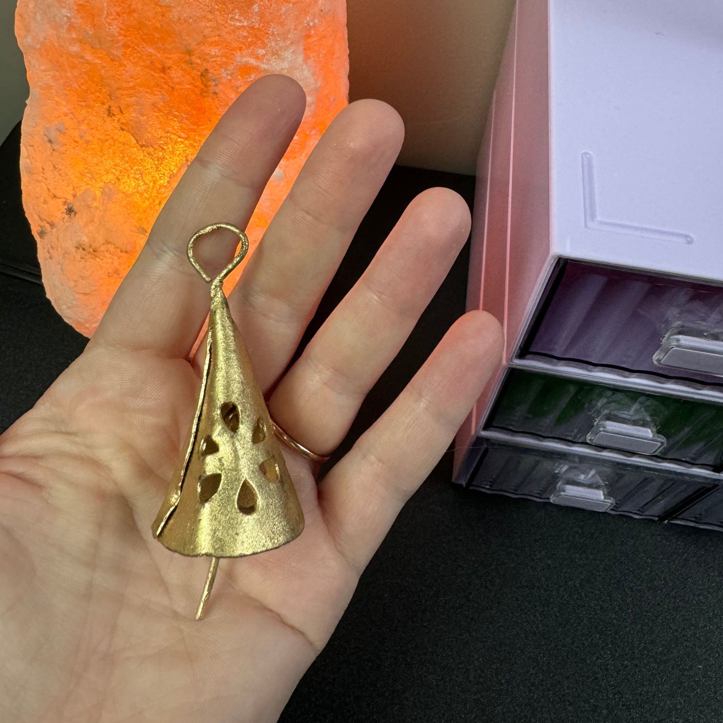 Hand holding a gold bell with a salt lamp in the background