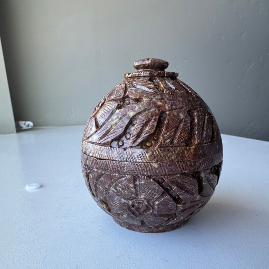 Soapstone decorative box with intricate carvings on a white surface.